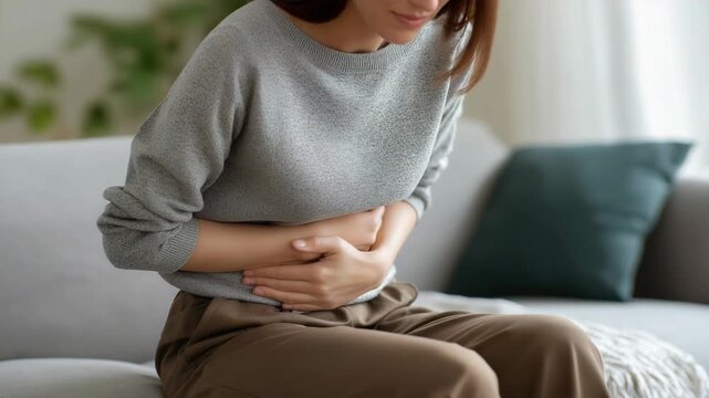 Woman at home rubbing her stomach in pain, representing abdominal discomfort, menstrual cramps, or digestive issues in a domestic setting, highlighting health and wellness concerns.