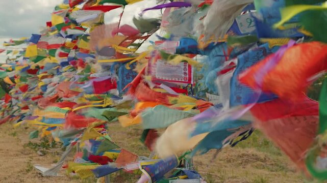 Close up of colorful Tibetan Buddhist prayer flags with mantras waving in the wind. A dynamic, spiritual scene with vibrant colors against a cloudy sky and field