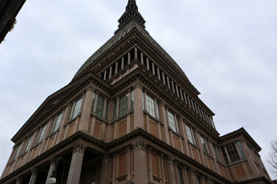 Maestosa veduta prospettica dal basso della Mole Antonelliana a Torino, simbolo dell'architettura eclettica e sede del Museo Nazionale del Cinema, sotto un cielo nuvoloso