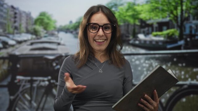 Woman points finger at book on street bridge while holding an open book and smiling; curiosity travel.