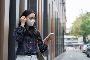 Fototapeta premium Young asian woman wearing face mask using smartphone outdoors