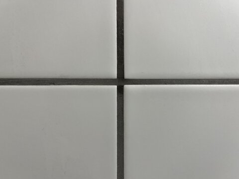 Perfect geometric cross intersection of clean white ceramic tiles with dark grey grout