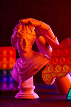 Classical greek sculpture bust with colorful neon lighting and pop it fidget toy composition