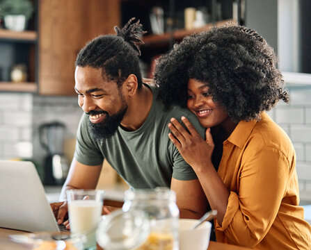 Happy young afro american couple having fun preparing food and looking for recipes online using a laptop in kitchen