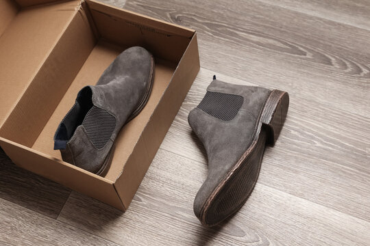 Pair of gray suede Chelsea boots with box on the floor. Men's shoes
