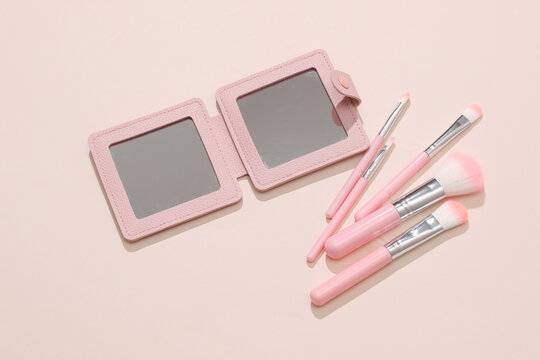 Pocket mirror and makeup brushes on a beige background. Beauty products