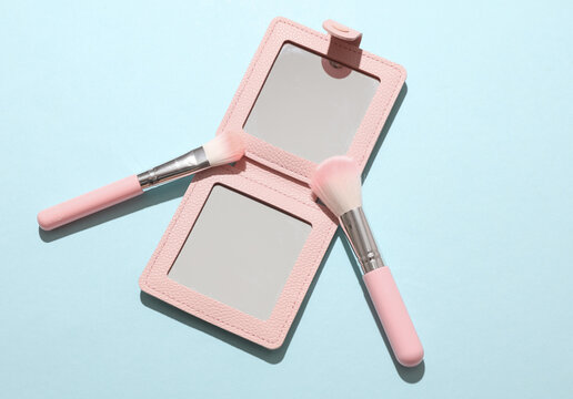 Pocket mirror and makeup brushes on a blue background. Beauty concept.