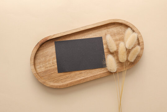 Black blank business card in Natural wooden tray with dry grass on beige background