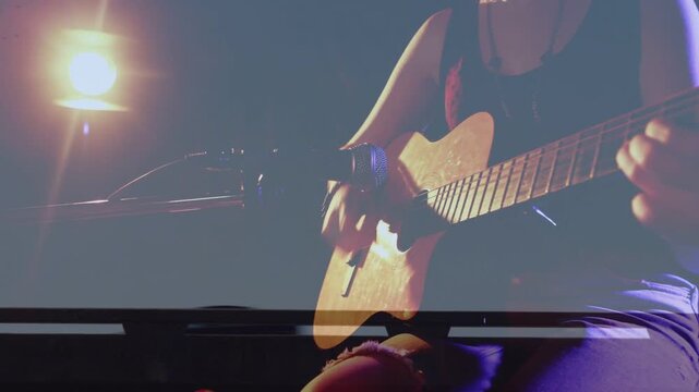 Camera panning bringing female musician to center guitar aligning with mic playing for acoustic set