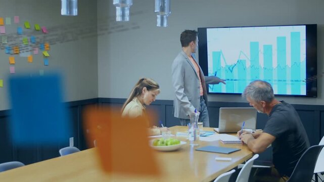 Presenter pointing at bar-line chart highlighting trends as business team writing notes, planning