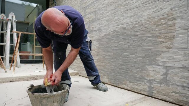 Skilled tiler using a sponge to clean a newly installed faux stone wall at a construction site
