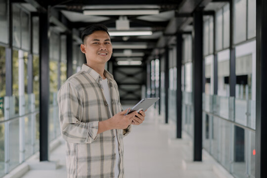 Young asian man smiles and bring tablet on his hand in the glass room. Working outdoor. Chilling Outside, Urban life. Moderm.