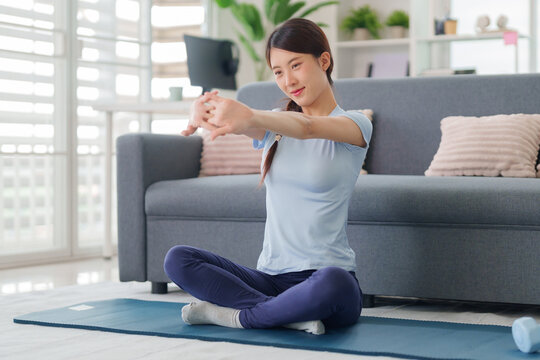 Asian adult woman stretching arms interlocking fingers practicing yoga exercise at home living room for health wellness body flexibility