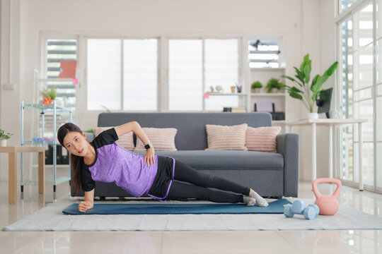 Asian young adult woman performing side plank exercise at home living room for fitness wellness strength core workout