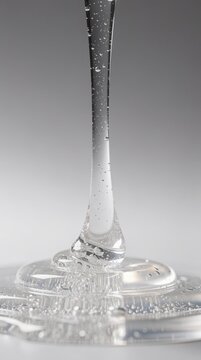 Clear viscous liquid with bubbles slowly dripping, captured in a close-up macro shot on a smooth surface.