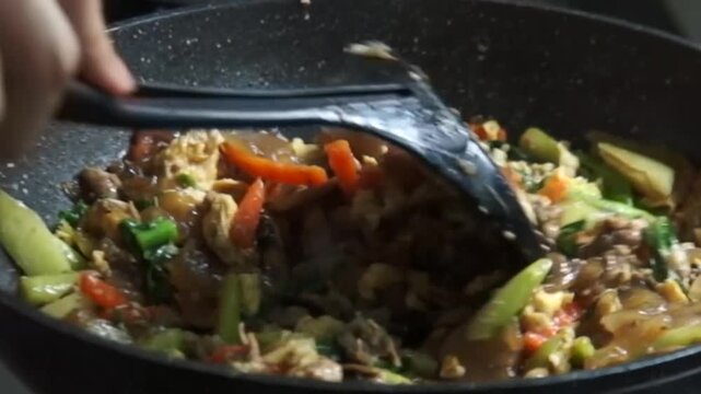 Final step cooking authentic Thai Pad See Ew at home. Chewy wide rice noodles stir-fried in a hot pan with tender marinated pork, egg, carrot, mushroom and Chinese broccoli, seasoned with savory dark 