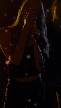 Vertical video: Camera rising, singer moving to mic, singing for music, particles overlaying frame