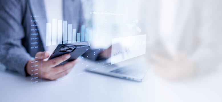 Person analyzing financial data and stock market charts on a smartphone overlayed with virtual graphics. While also having a laptop visible. Representing modern investment and digital finance concepts