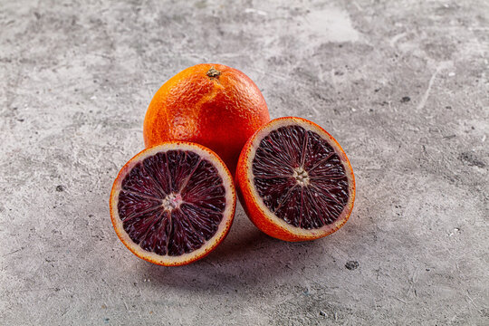 Fresh ripe blood orange, whole and sliced in half on a textured gray background