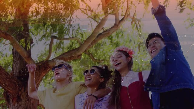 Vertical video: Sunlight through leaves sparking friends raising arms, cheering under warm overlay