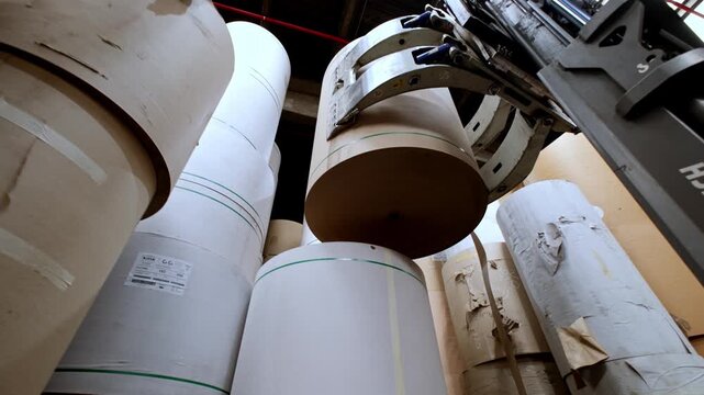 Forklift handling and stacking large paper rolls inside a paper manufacturing facility. The scene highlights industrial logistics, material handling, warehouse operations,efficient production workflow
