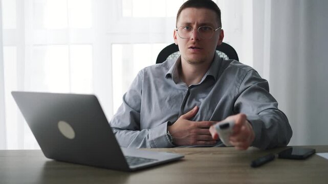 Turning on a heater in a cold office space.
A man uses a remote control to turn on an air conditioner to warm up an office.