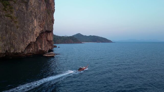 Koh Muk, Thailand: Aerial drone footage of a long-tail boat sailing by the dramatic cliff of the Koh Mook island in the Andaman sea in Trang province in southern Thailand in late afternoon