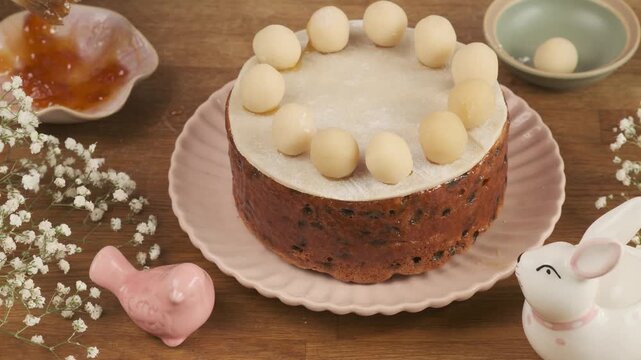 A woman decorates a British Easter cake, Simnel, with marzipan balls on a wooden table. Step-by-step video recipes. Horizontal video. Happy Easter.