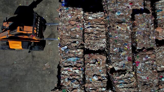 Top-down drone view of a paper recycling yard with machinery handling compressed paper bales, showing loading, storage and logistics operations in an outdoor industrial environment.