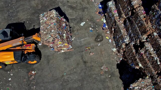 Top-down drone view of a paper recycling yard with machinery handling compressed paper bales, showing loading, storage and logistics operations in an outdoor industrial environment.