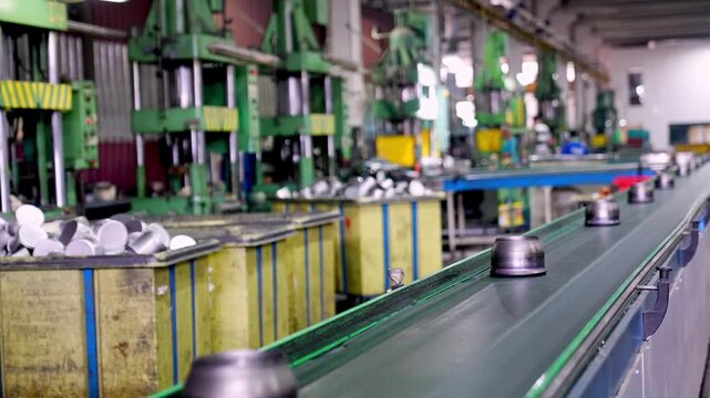 Metal pot components moving along a conveyor belt in a factory, showing automated cookware production line, mass manufacturing process and industrial equipment in a modern metal facility