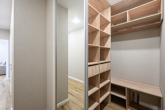 modern walk-in closet with light wood shelving, open compartments, hanging rod, built-in bench, neutral wall finish