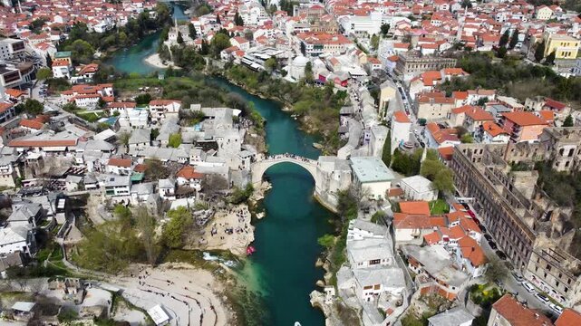 Old bridge above Neretva river in Mostar, Bosnia and Herzegovina. People crossing Old bridge, aerial drone view. 