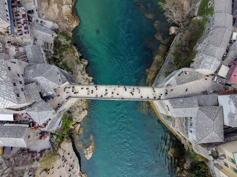 Old bridge above Neretva river in Mostar, Bosnia and Herzegovina. People crossing Old bridge, aerial drone view. 
