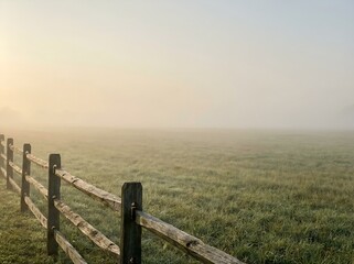 Fototapeta premium Foggy Field with a Wooden Fence and Morning Mist Under a Soft Sunrise Glow
