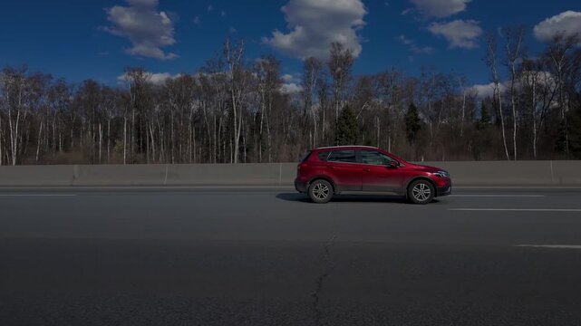 Red Crossover Driving on Highway Through Birch Forest on Sunny Day