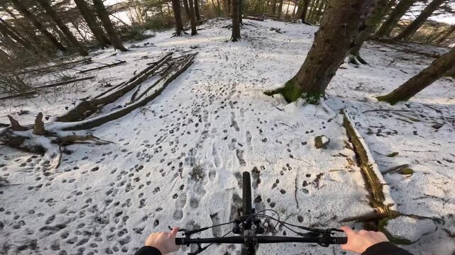 Action camera footage capturing an enduro cross-country mountain biker riding through a Scandinavian forest covered in snow. The scene highlights winter trail conditions, flowing movement, and technic