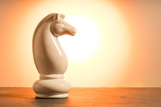 Chess knight standing on table against orange background, strategy and game concept
