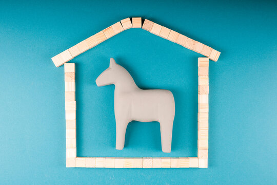 Gray wooden toy horse enclosed in house-shaped frame with chimney, confinement and home concept