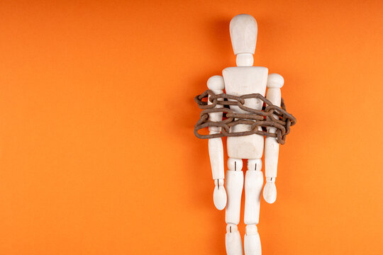 Artist doll tied with metal chain on orange background, restraint and loss of freedom theme