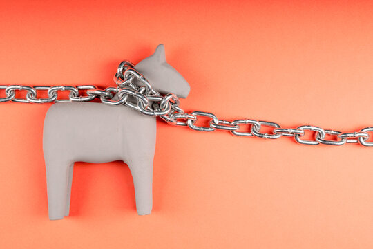 Gray wooden toy horse on orange surface with chain around neck, tether and control concept