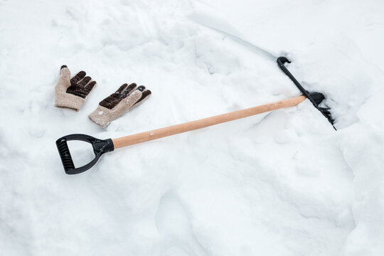 A snow shovel and gloves to protect your hands from frostbite are in the snow