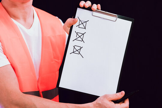 Worker in safety vest holds clipboard with cross marks and pen.