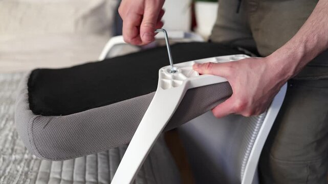 Adult male assembling office chair using hex key tool on wooden floor. Caucasian man hands screw chair lifting mechanism. Assembling office chair.