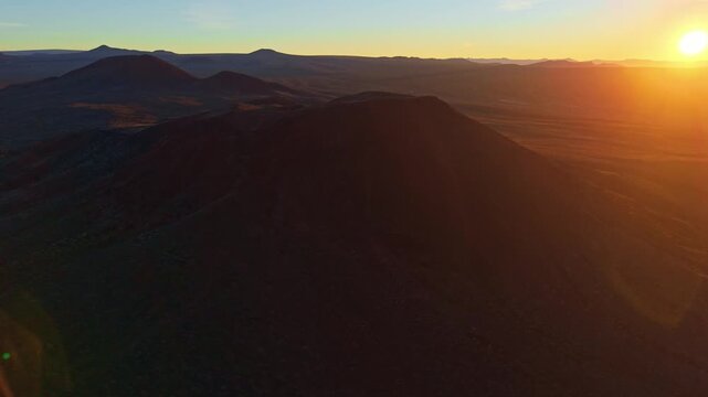 Scenic aerial perspective of volcanic cinder cones in Mojave Desert illuminated by golden sunrise light