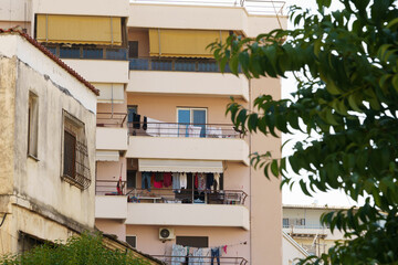 Fototapeta premium Urban scene of an apartment complex with laundry drying on balconies. Beige buildings, yellow awnings, and green leaves in the foreground create a candid, slice-of-life mood under natural light.