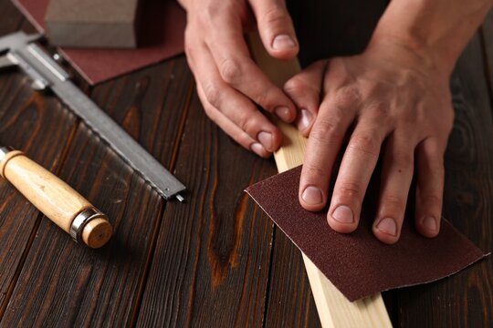 Man polishing wooden plank with sandpaper at table, closeup