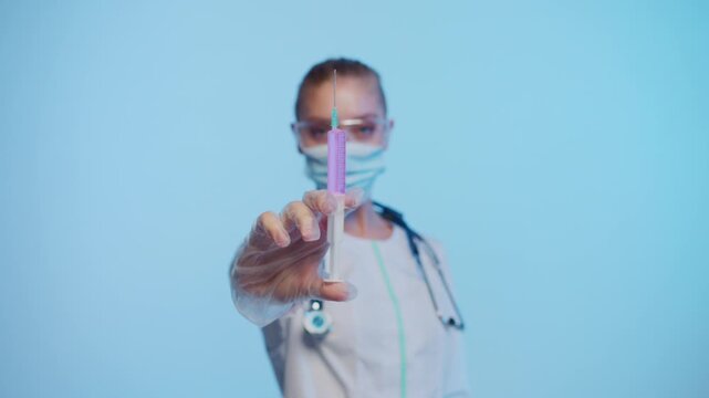 Female doctor wearing a protective mask holding a syringe with purple liquid vaccine for immunization and vaccination