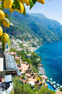 Picturesque view of Positano on Amalfi Coast, Italy, with colorful hillside houses overlooking Mediterranean Sea. Bright yellow lemons hang in foreground. Welcome to Positano concept image