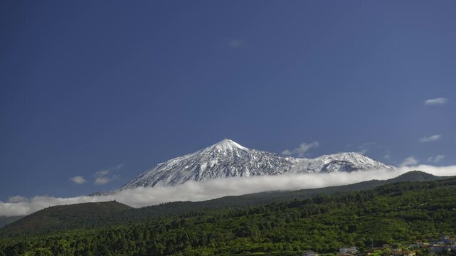 4K time-lapse video showing white clouds dramatically flowing and wrapping around the snow-covered summit of Mount Teide, the highest peak in Spain. Filmed in Teide National Park on Tenerife